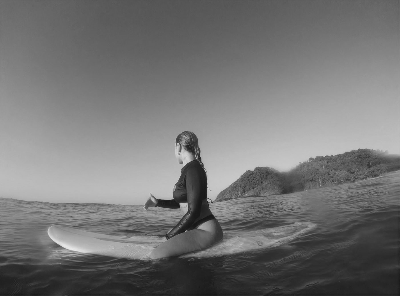 Thayná sentada na prancha no mar